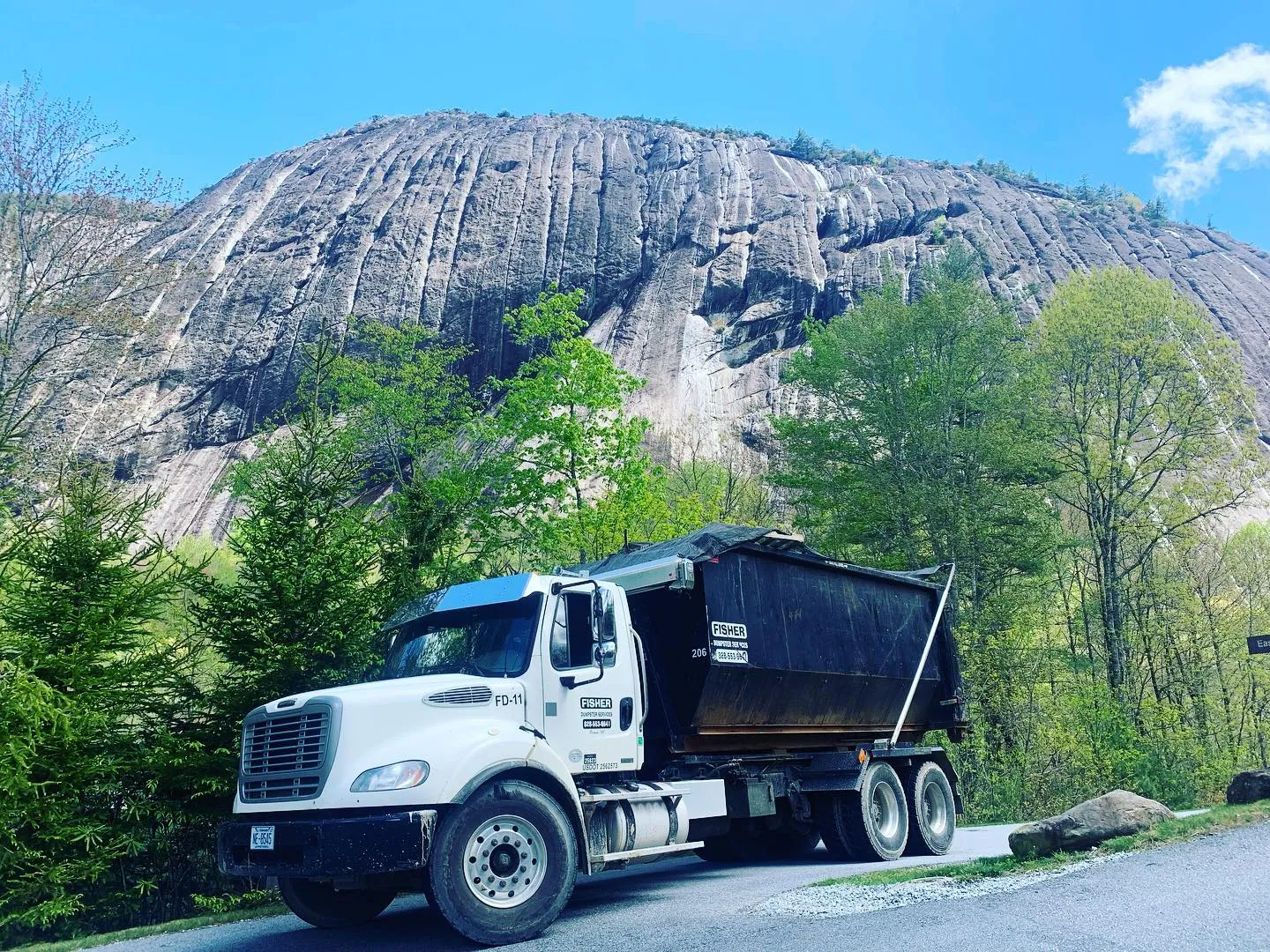 Dump truck parked near a large rocky cliff and green trees.